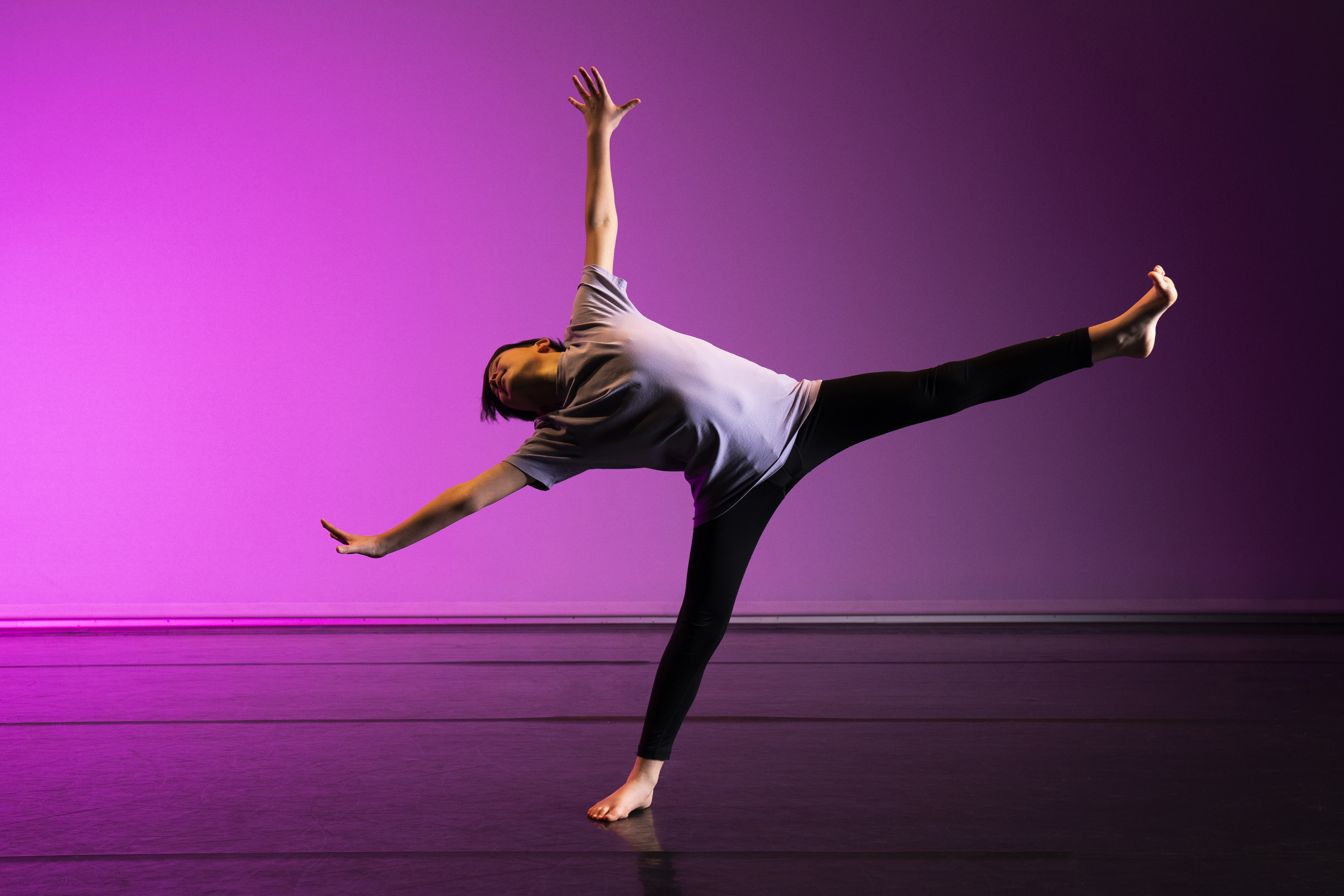 An image from a photoshoot. One male student is falling off one leg whist reaching all his limbs away from his body. He is again a light purple background.