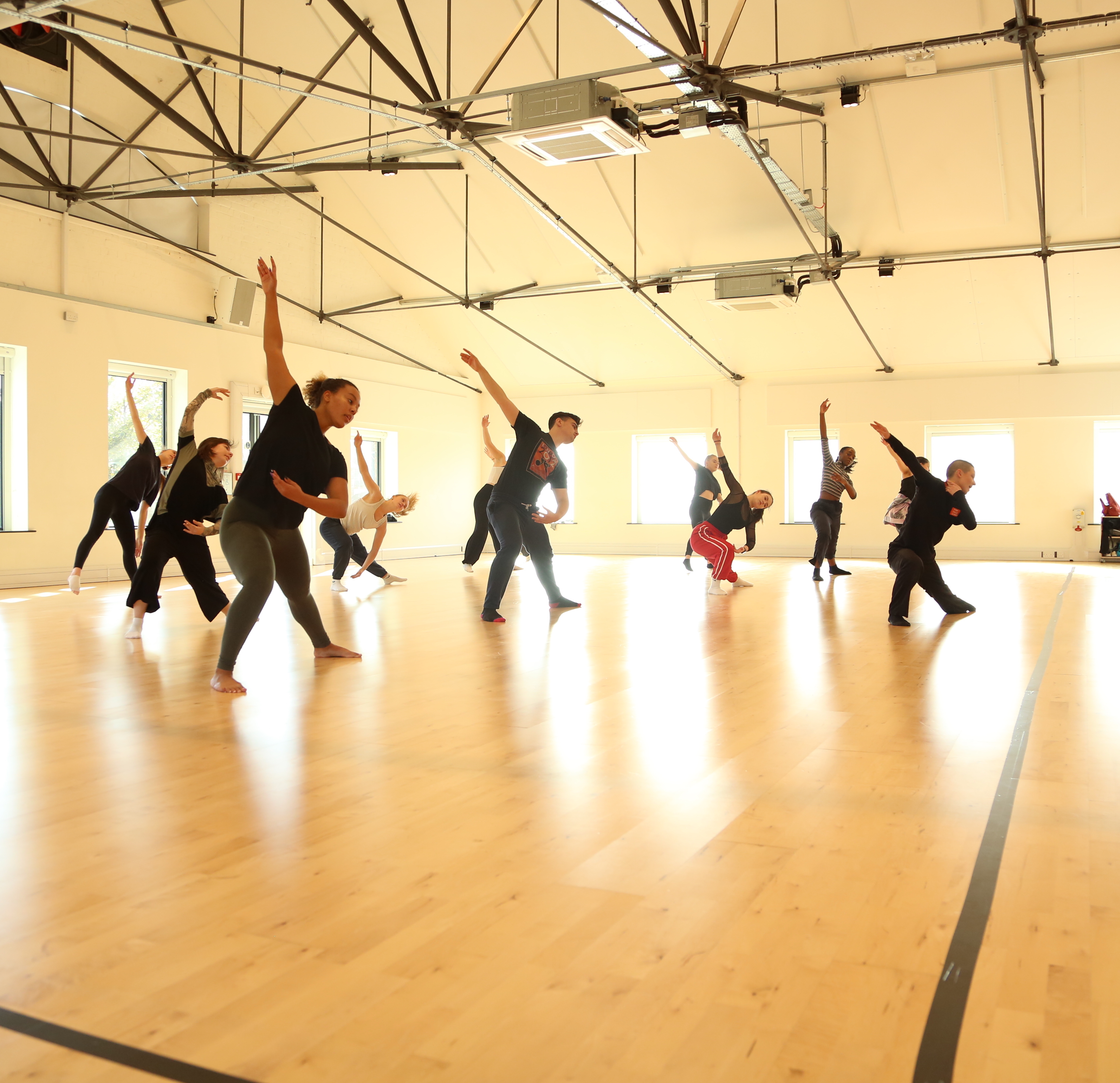 A class of students working in the studio with legs outstretched, and one arm raised in the air.